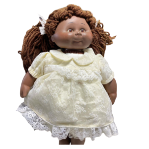 Vintage 1983 African American Cabbage Patch Kid Doll named Sally with Xavier Roberts signature, brown yarn pigtails, wearing a yellow lace dress, embodying the classic charm of early Cabbage Patch dolls.